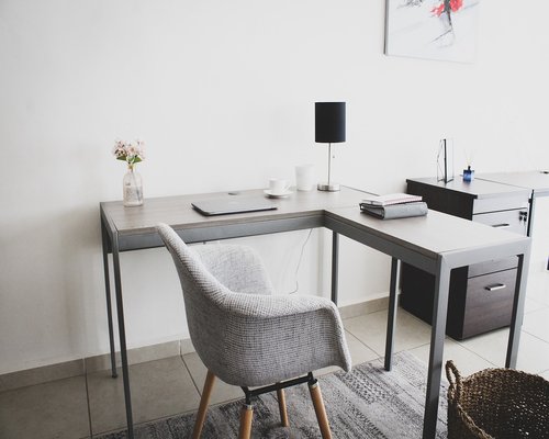 A laptop on a clean wooden desk with a notebook nearby